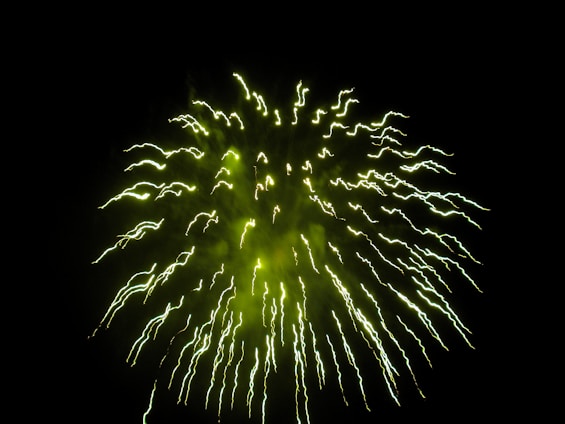 A dazzling burst of neon green and gold fireworks exploding against a black sky, with subtle smoke and sparks glowing around.