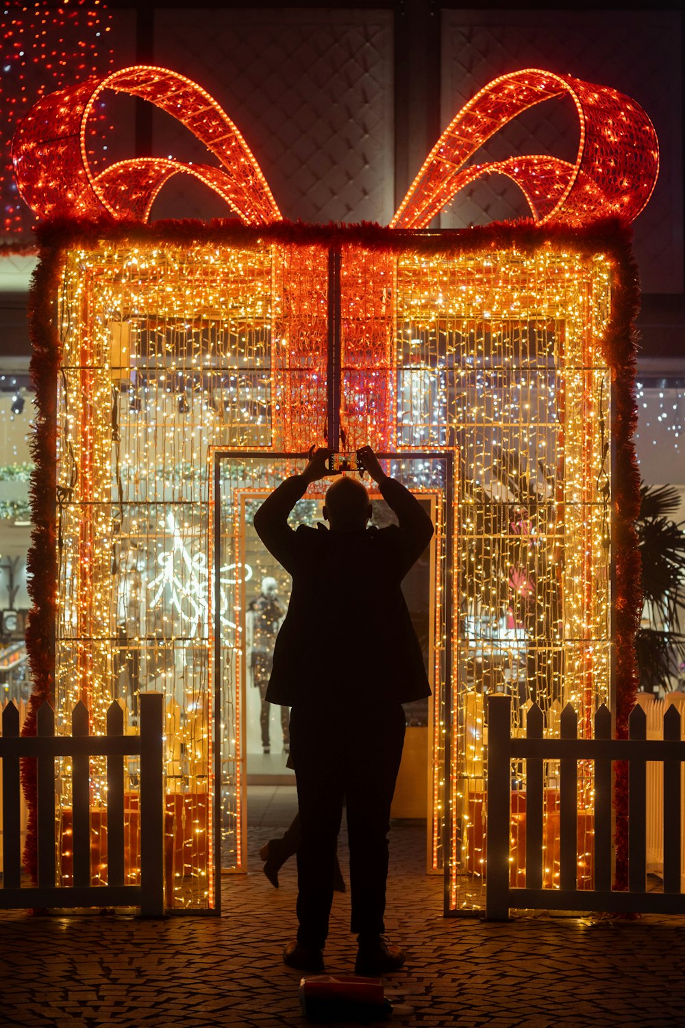 man in black coat standing near white and red floral arch