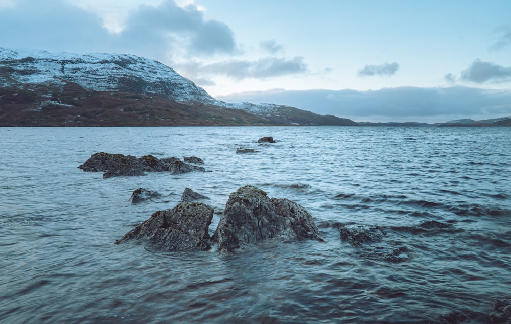 gray rocky shore near green mountain under white cloudy sky during daytime