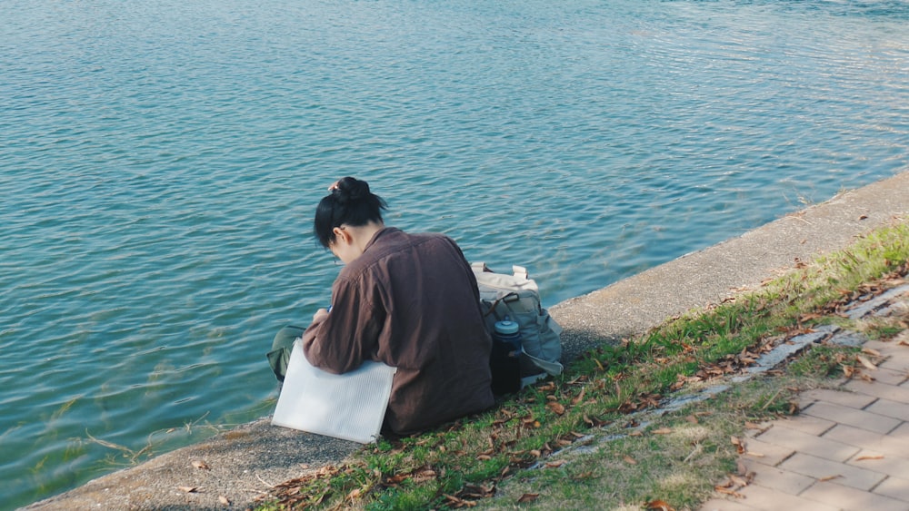 woman in brown shirt sitting on white concrete bench near body of water during daytime