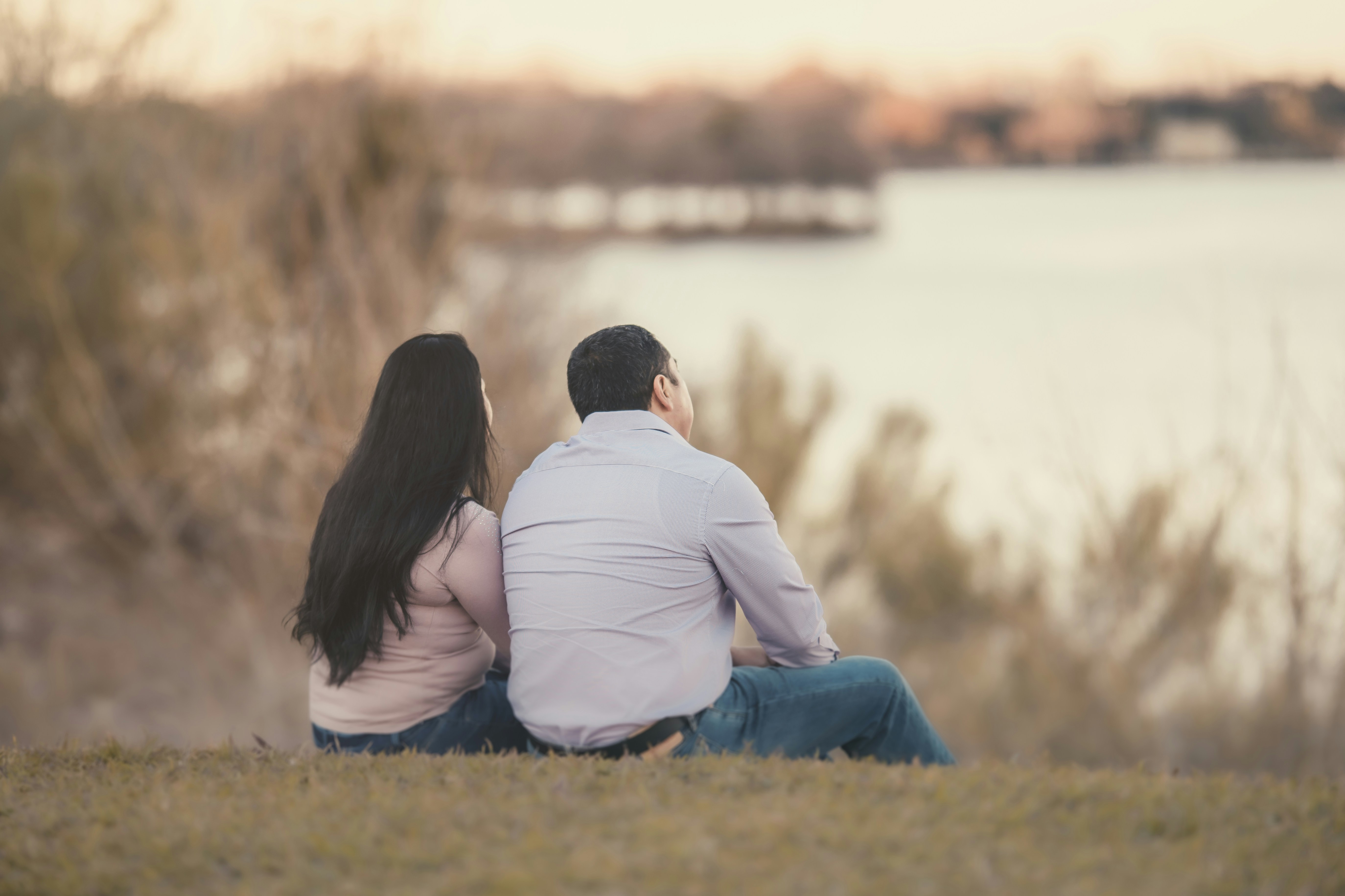 couple sitting on grass field near body of water during daytime