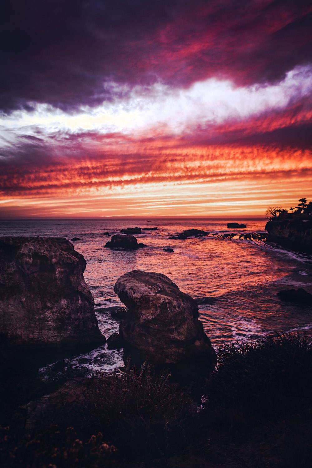 silhouette of rocks on sea shore during sunset