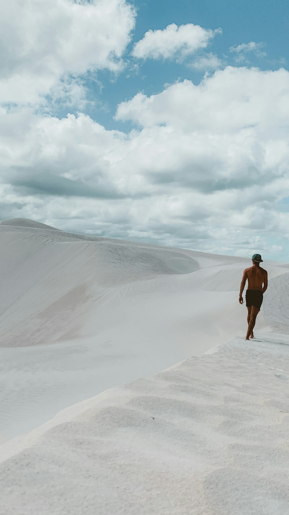 woman in black tank top standing on gray sand under white clouds during daytime