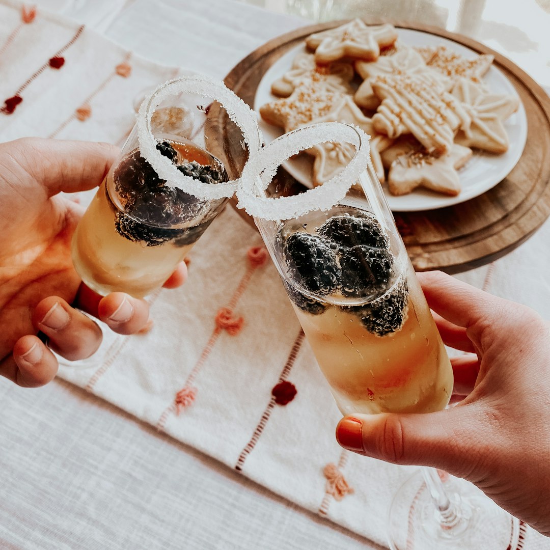 person holding clear drinking glass with brown liquid