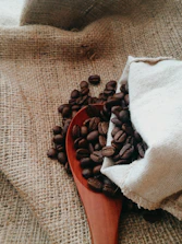Artisan ceramic spoons resting on a cream-colored linen cloth beside coffee beans.