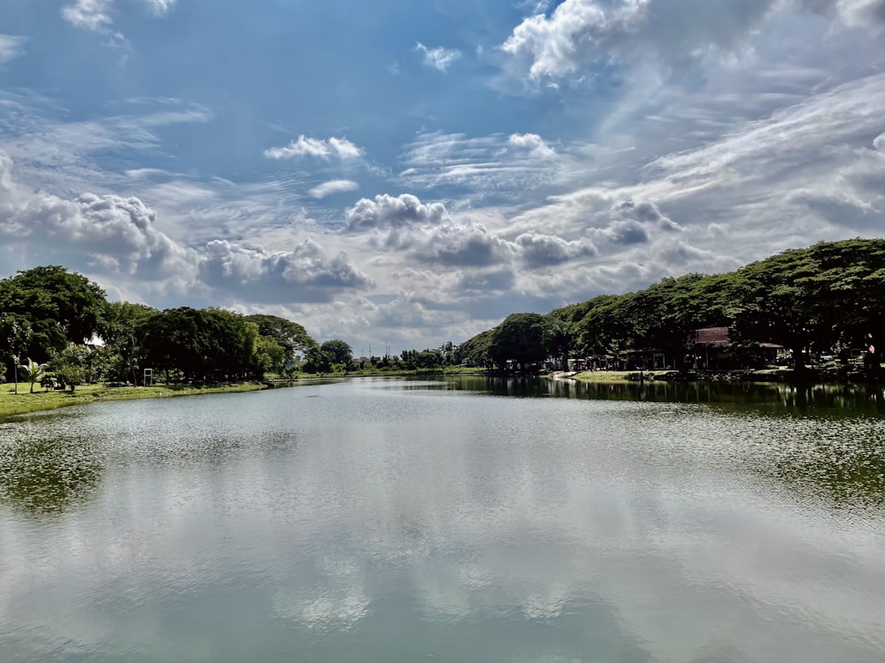 昼間は青空と白い雲の下、川沿いの緑の木々