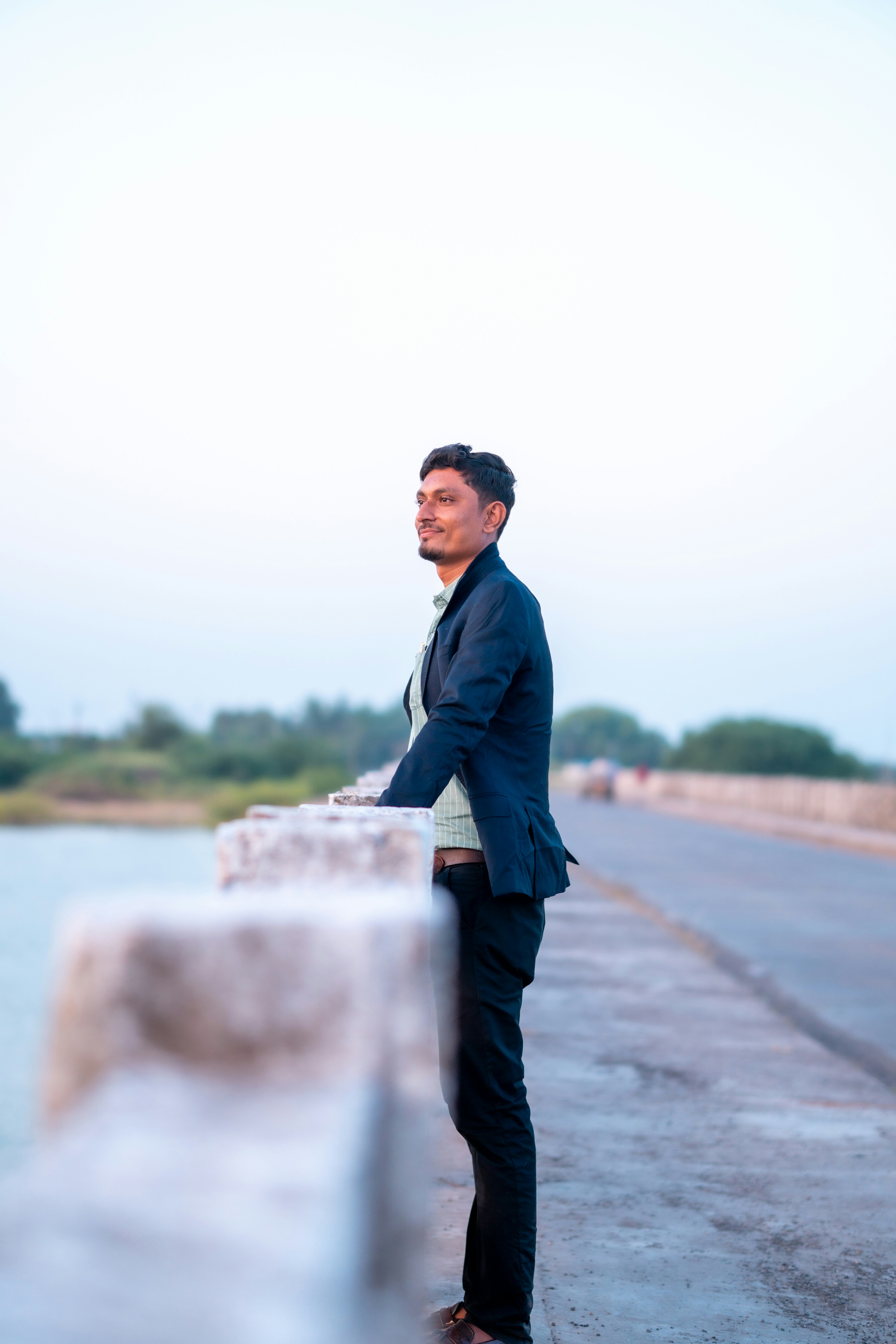 Fotomural man in gray jacket standing on gray concrete pavement near body of water during daytime