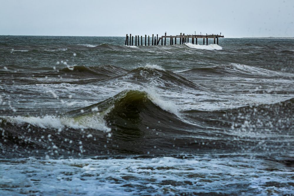 sea waves crashing on wooden dock during daytime