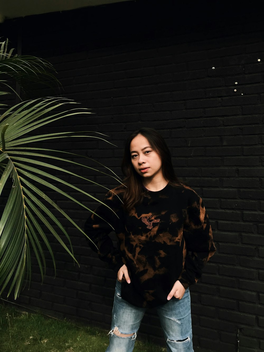 woman in black and brown long sleeve shirt standing beside green plant