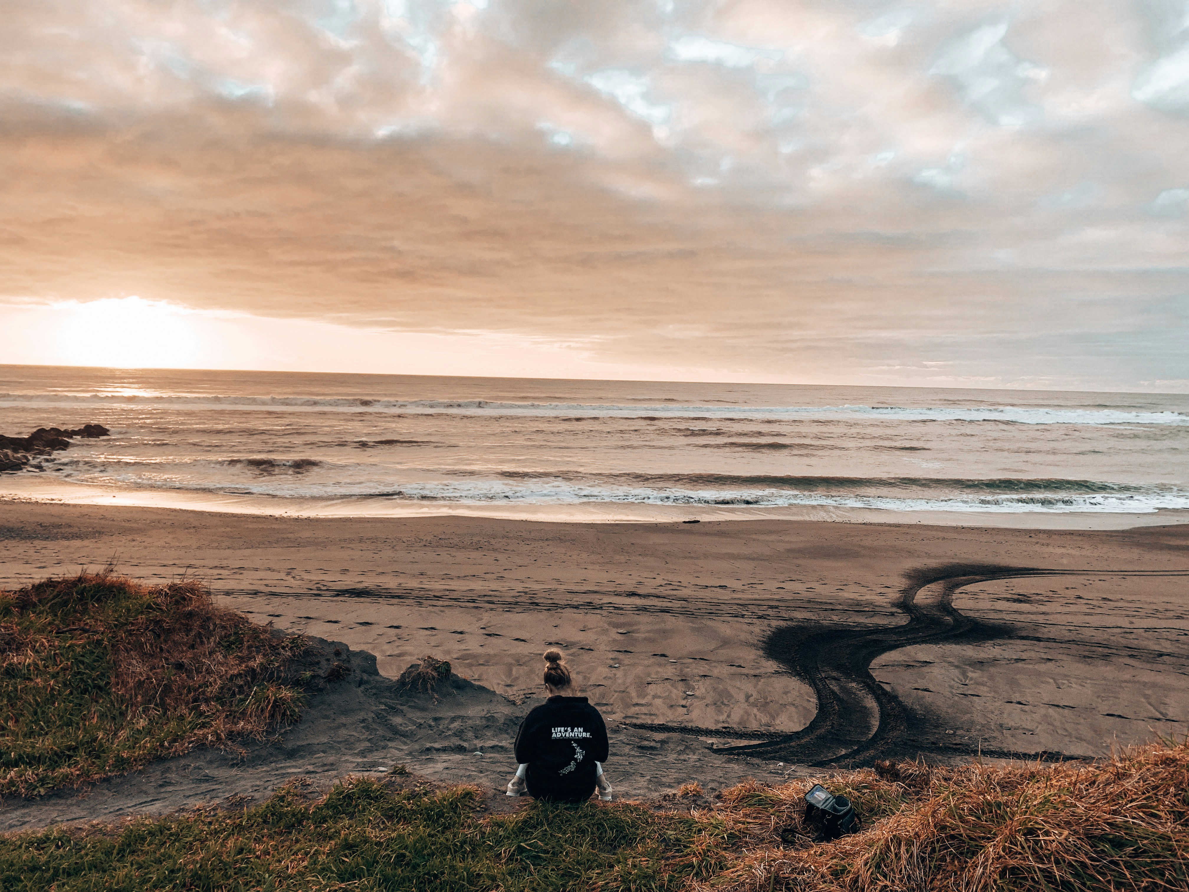 person in black jacket sitting on brown rock near sea during daytime