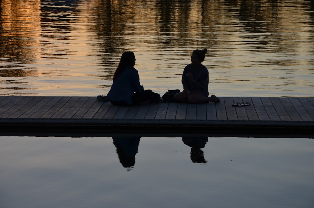 2 Personen sitzen während des Sonnenuntergangs auf dem Dock