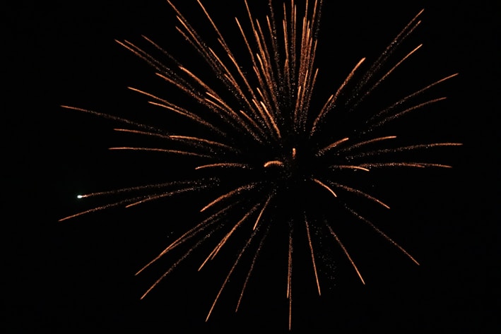 A fiery chrysanthemum burst in metallic gold and neon green sparks against a black sky