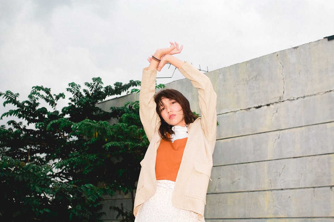 woman in white long sleeve shirt and white skirt standing beside gray concrete wall during daytime