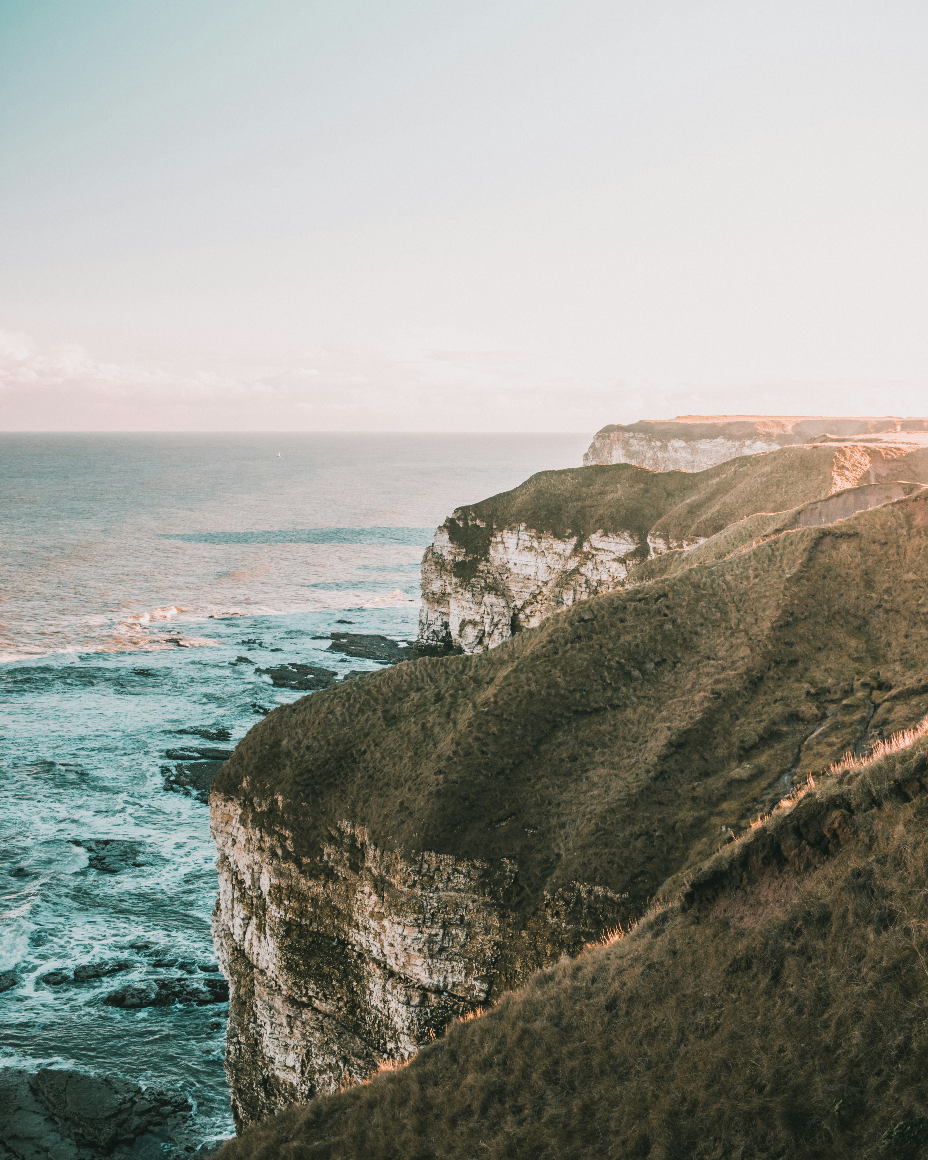 brown and green mountain beside blue sea under blue sky during daytime