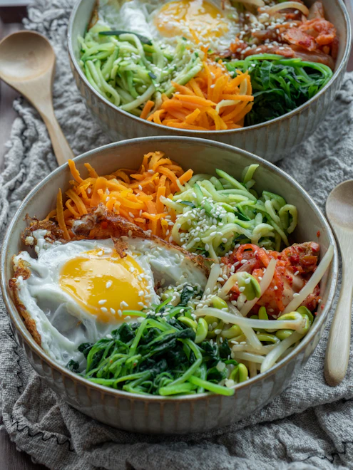 Close-up of freshly made bibimbap with colorful vegetables and a sunny-side-up egg on top.