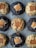 An arrangement of nine cookies on a baking sheet. The cookies are of two varieties: some are darker and others are lighter in color. Each cookie has a distinct filling of a marshmallow and a rectangular biscuit piece pressed into the center.