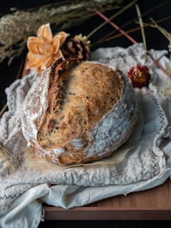 A rustic loaf of bread on a linen cloth, surrounded by scattered grains and seeds.