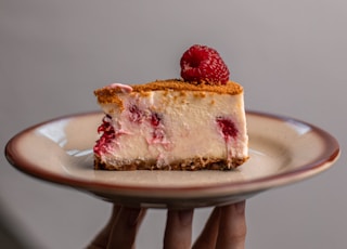 person holding strawberry cake on white ceramic plate