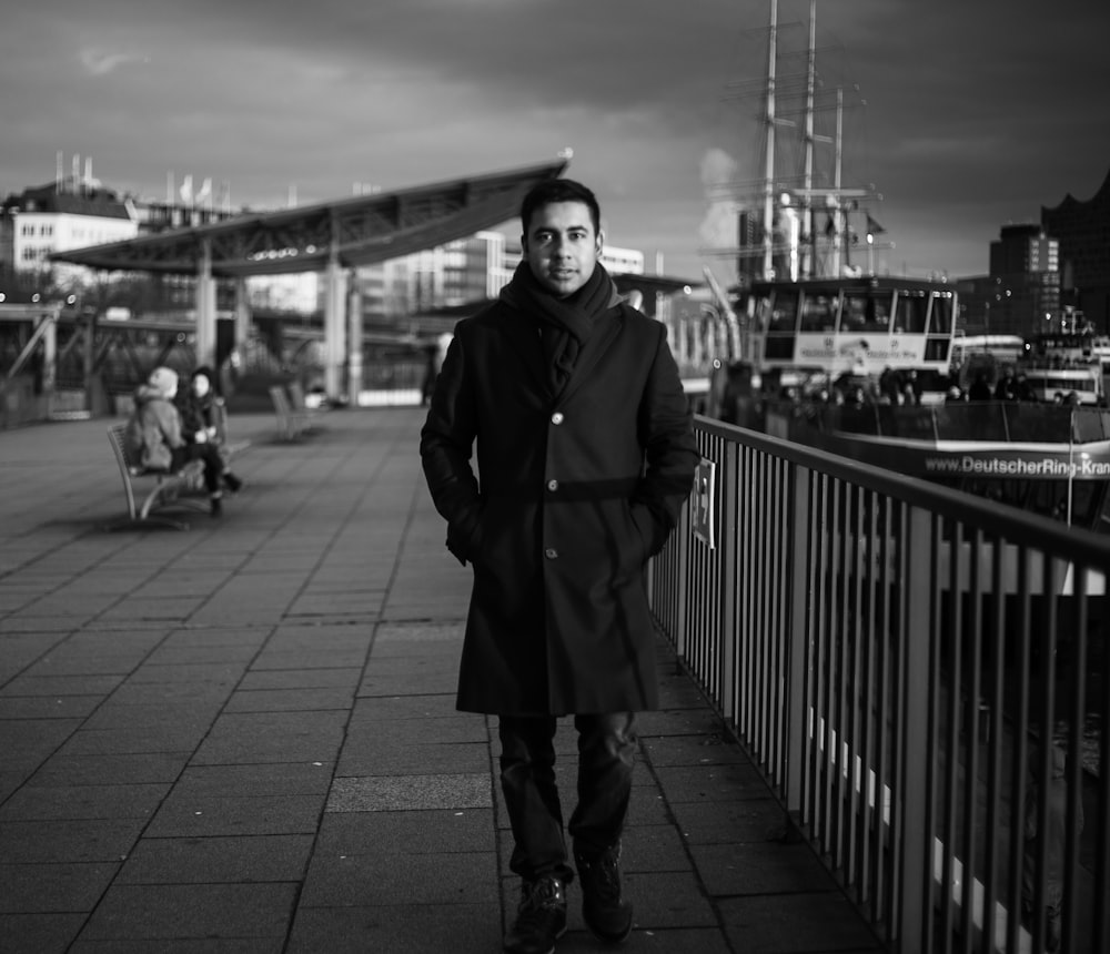 woman in coat standing on sidewalk in grayscale photography