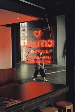 man in black jacket and black pants standing near red and white neon sign