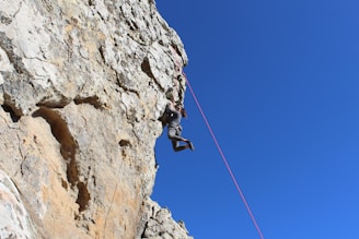 A climber scaling a steep rock face against a clear blue sky.