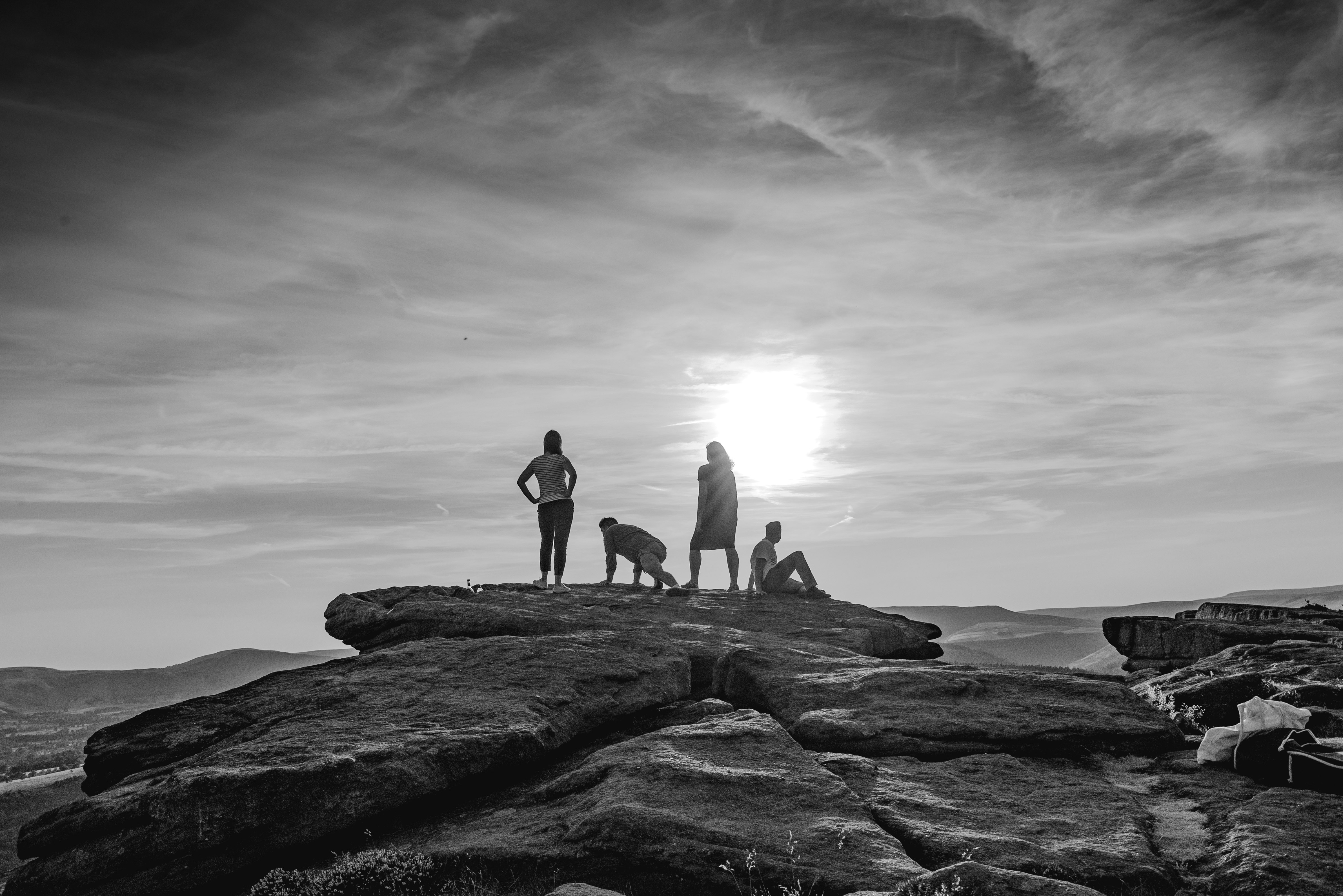 silhouette of 3 people standing on rock formation near body of water during daytime
