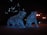 Two bear sculptures covered in blue lights are situated in an outdoor setting, illuminated against the dark night. Surrounding the sculptures are glowing streetlights, enhancing the night-time ambiance. The bears appear to be walking forward.