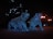 Two bear sculptures covered in blue lights are situated in an outdoor setting, illuminated against the dark night. Surrounding the sculptures are glowing streetlights, enhancing the night-time ambiance. The bears appear to be walking forward.