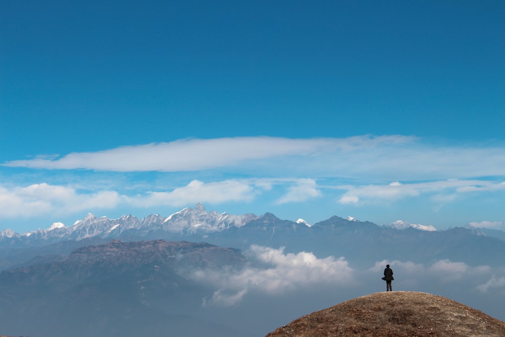 person standing on rock formation near snow covered mountains during daytime