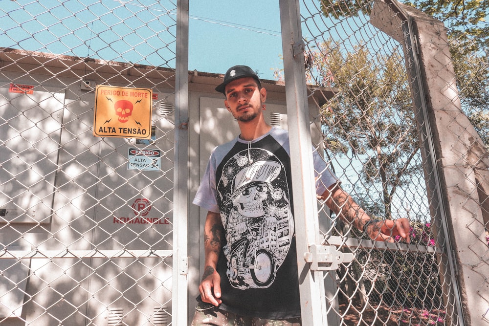 man in black and white crew neck t-shirt standing beside white metal fence during daytime