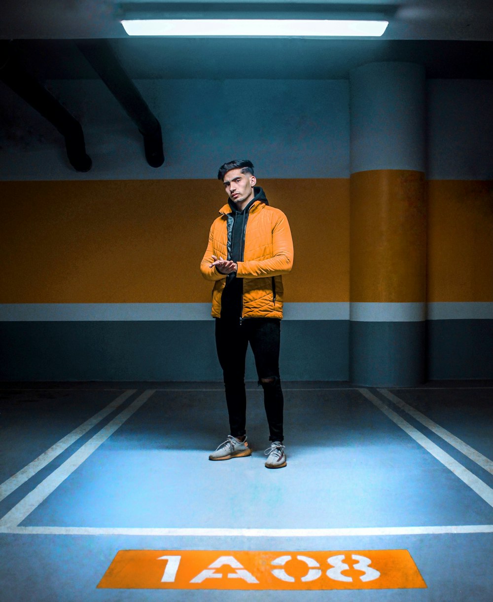 man in yellow polo shirt and black pants standing beside yellow and blue wall