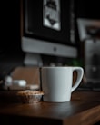 white ceramic mug beside brown round biscuit