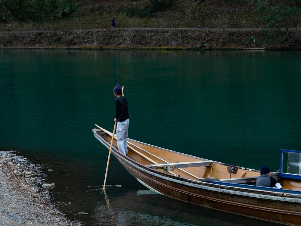 man in black jacket and blue denim jeans standing on brown wooden boat on river during
