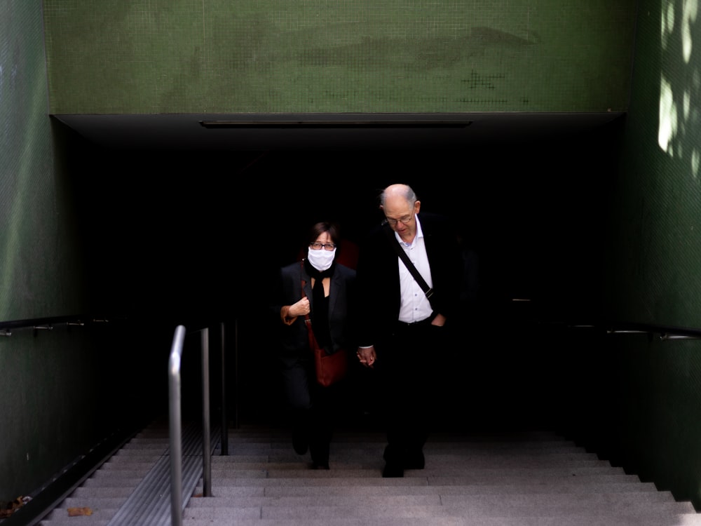 man in black suit jacket and black pants standing beside green wall