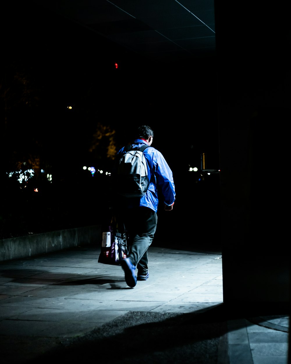 man in blue jacket and black pants walking on sidewalk during night time