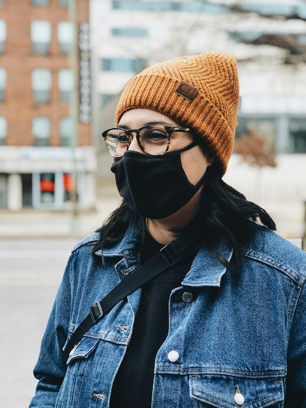 woman in blue denim jacket wearing black framed eyeglasses and brown knit cap