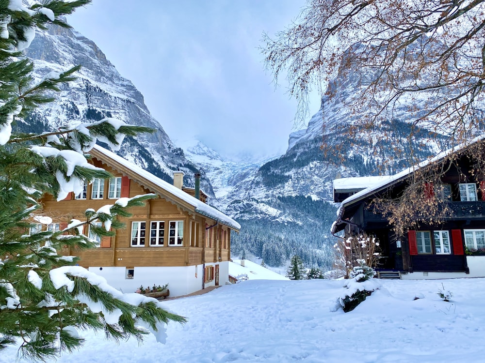 casa de madeira marrom no chão coberto de neve perto da montanha coberta de neve durante o dia