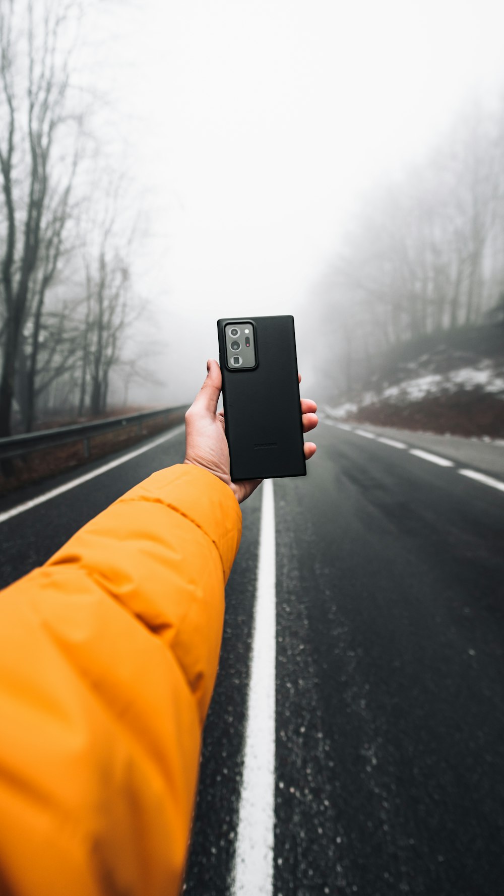 person in orange jacket holding black smartphone