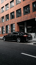 black sedan parked beside brown concrete building during daytime