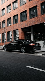 black sedan parked beside brown concrete building during daytime