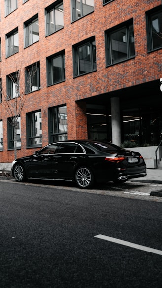 black sedan parked beside brown concrete building during daytime