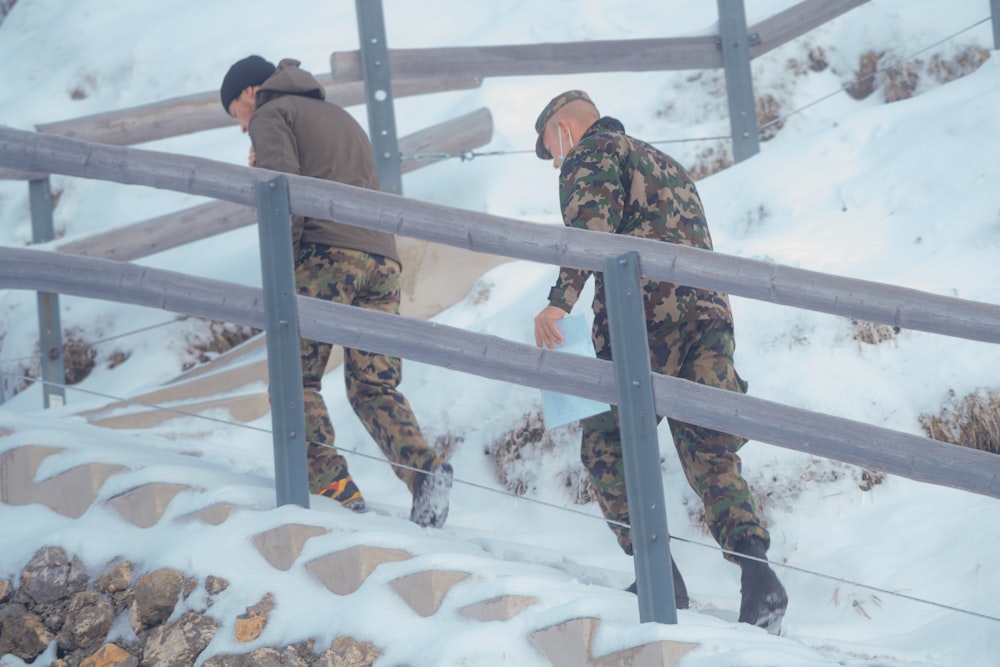 man in green and brown camouflage jacket and black pants standing on snow covered ground during