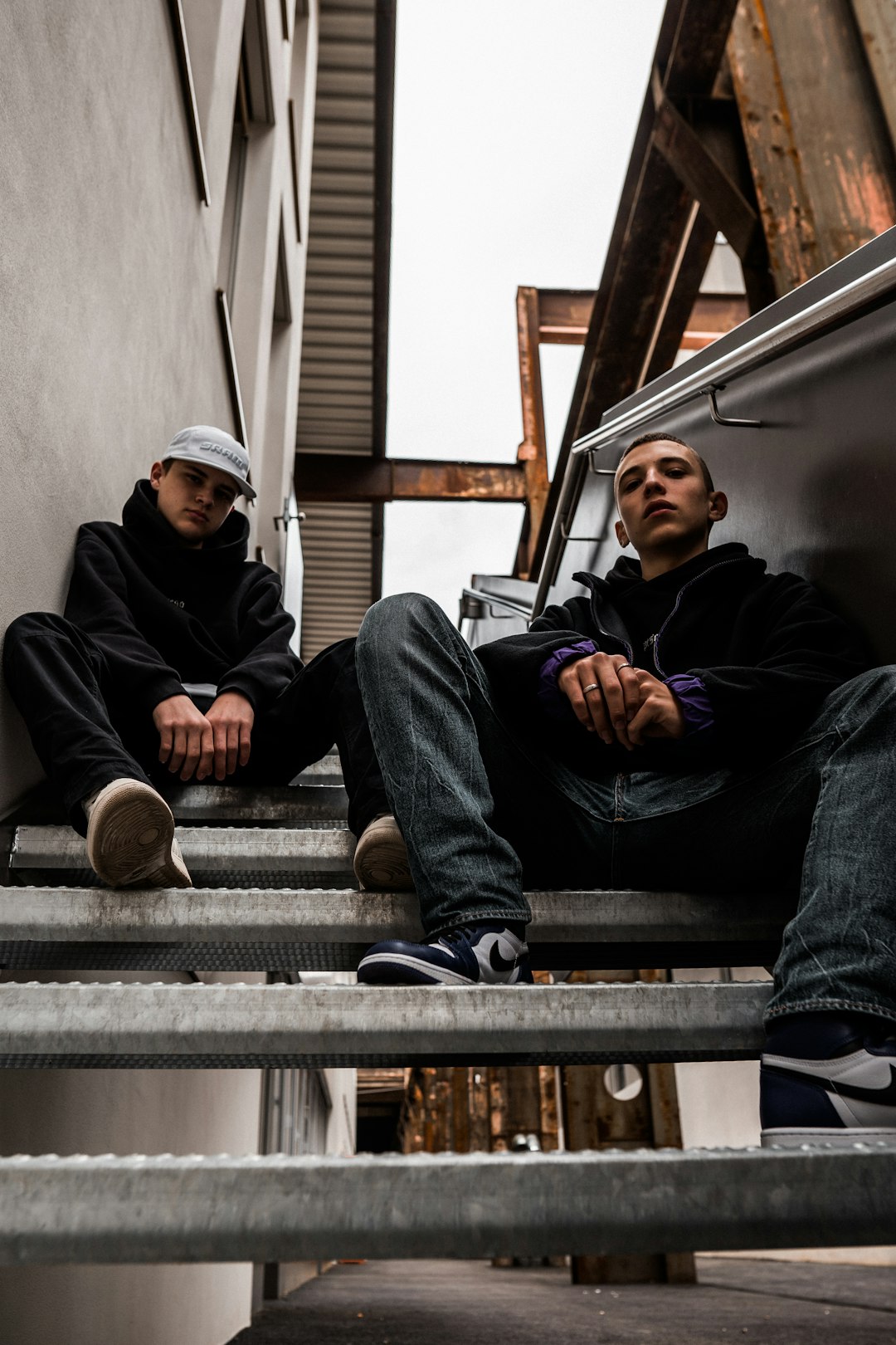 man in black jacket and blue denim jeans sitting on stairs