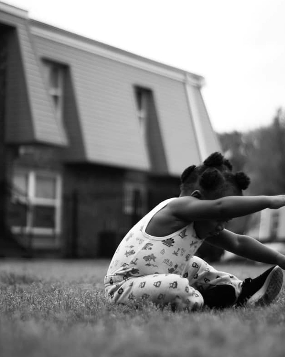 grayscale photo of woman in tank top and pants sitting on grass field