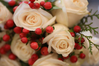 Close-up of a bouquet with bordeaux blooms, ivory roses, and sage green leaves tied with a light gold ribbon.