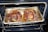 Two large, roasted pork knuckles situated in a foil tray inside an oven. The meat appears well-cooked, with a rich brown color and crispy exterior.