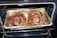 Two large, roasted pork knuckles situated in a foil tray inside an oven. The meat appears well-cooked, with a rich brown color and crispy exterior.