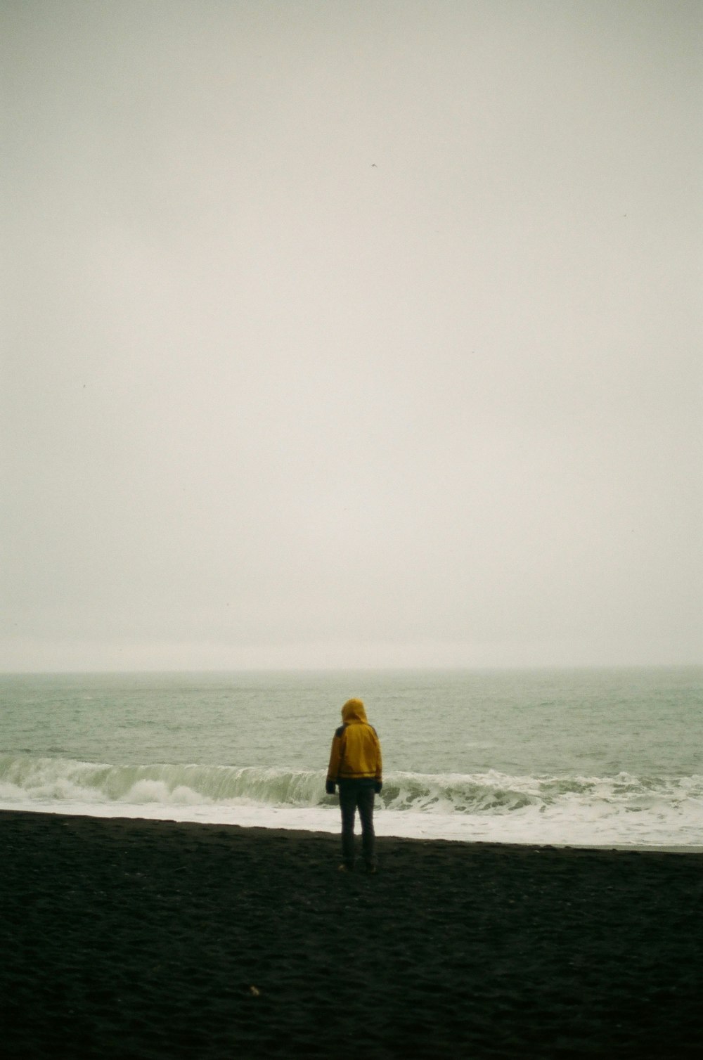 man in yellow jacket standing on beach during foggy weather