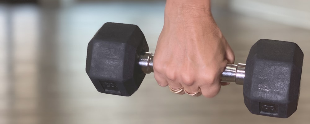 person holding black dumbbell on brown wooden table