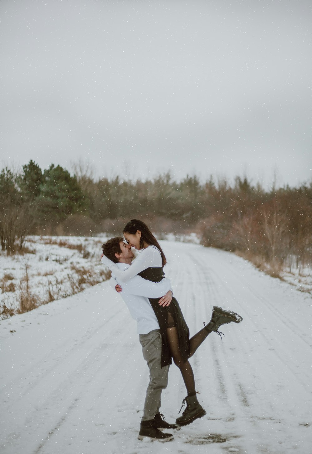 woman in white jacket and brown pants carrying brown short coated dog on snow covered field